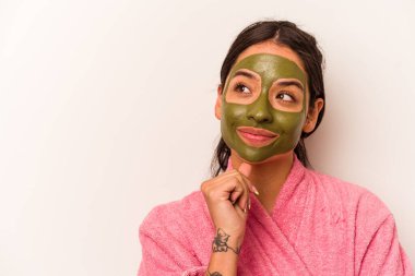 Beyaz arka planda izole edilmiş yüz maskesi takan genç İspanyol kadın şüpheli ve şüpheci bir ifadeyle yana bakıyor..