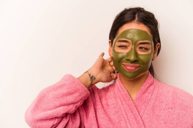 Yüz maskesi takan genç İspanyol kadın beyaz arka planda izole edilmiş kafasının arkasına dokunuyor, düşünüyor ve bir seçim yapıyor..