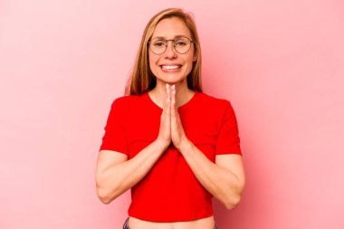 Pembe arka planda soyutlanmış genç beyaz bir kadın el ele tutuşup ağzının kenarında dua ediyor, kendinden emin hissediyor..