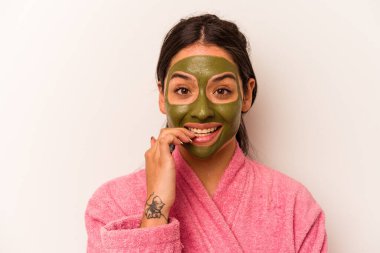 Beyaz arka planda izole edilmiş, tırnak yiyen, gergin ve endişeli bir yüz maskesi takan genç İspanyol kadın..