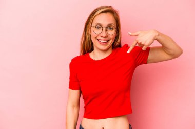 Pembe arka planda izole edilmiş genç beyaz bir kadın gömlek fotokopisini elle gösteriyor, gururlu ve kendinden emin.