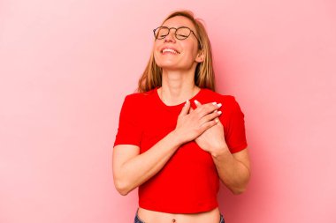 Pembe arka planda izole edilmiş genç beyaz bir kadın, dostane bir ifadeye sahip, avuçlarını göğsüne bastırıyor. Aşk konsepti.