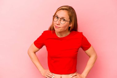Pembe arka planda izole edilmiş genç beyaz kadın kafası karışmış, kuşkulu ve güvensiz hissediyor..