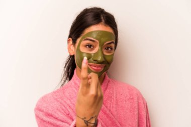 Beyaz arka planda izole edilmiş yüz maskesi takan genç İspanyol kadın sanki seni davet ediyormuş gibi seni işaret ediyor..