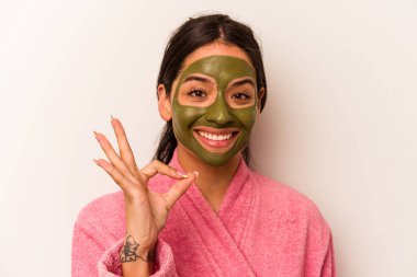 Yüz maskesi takan genç İspanyol kadın beyaz arka planda izole edilmiş neşeli ve kendinden emin bir şekilde iyi niyet gösteriyor..