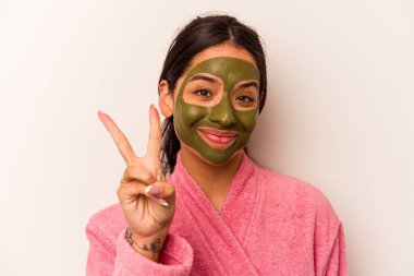 Yüz maskesi takan genç İspanyol kadın beyaz arka planda iki numarayı parmaklarıyla gösteriyor..