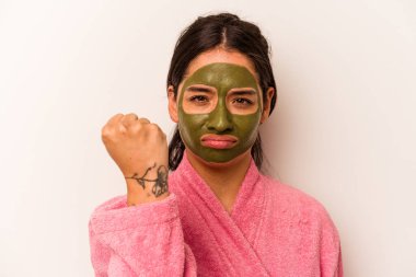 Beyaz arka planda izole edilmiş yüz maskesi takan genç İspanyol kadın yumruğunu kameraya gösteriyor, agresif yüz ifadesi..