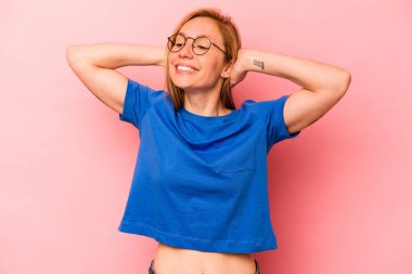 Pembe arka planda soyutlanmış genç beyaz bir kadın kendini güvende hissediyor, elleri başının arkasında..