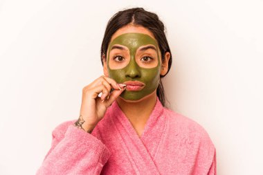 Yüz maskesi takan genç İspanyol kadın beyaz arka planda izole edilmiş ve parmakları dudaklarında bir sır saklıyor..