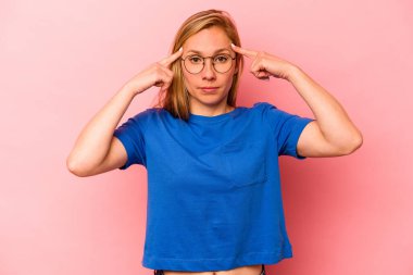 Pembe arka planda izole edilmiş genç beyaz kadın bir göreve odaklanmış, parmaklarını işaret ediyor..