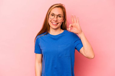 Genç beyaz kadın pembe arka planda izole edilmiş neşeli ve kendinden emin, iyi bir jest yapıyor..