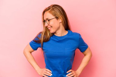 Pembe arka planda izole edilmiş beyaz bir kadın. Kendine güveni tam. Kalçalarını tutuyor..