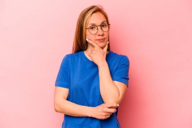 Pembe arka planda izole edilmiş genç beyaz kadın şüpheli, belirsiz, seni muayene ediyor..