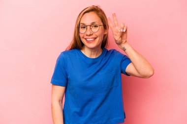 Pembe arka planda izole edilmiş genç beyaz kadın iki numarayı parmaklarıyla gösteriyor..