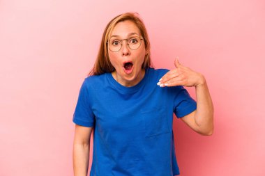 Pembe arka planda izole edilmiş genç beyaz kadın bir şeye gülüyor, elleriyle ağzını kapatıyor..