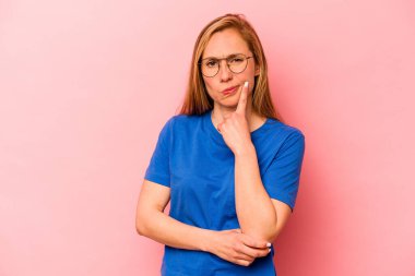 Pembe arka planda izole edilmiş genç beyaz kadın alaycı bir ifadeyle kameraya bakıyor..