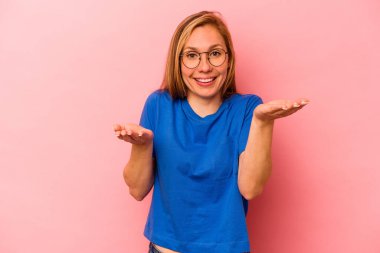 Pembe arka planda izole edilmiş genç beyaz kadın kollarıyla ölçek oluşturuyor, mutlu ve kendinden emin hissediyor..