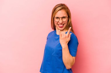 Pembe arka planda izole edilmiş genç beyaz kadın parmaklarıyla taş hareketi gösteriyor.