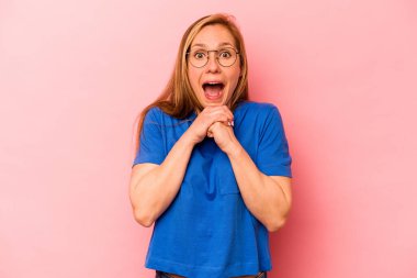 Pembe arka planda izole edilmiş genç beyaz bir kadın şans için dua ediyor, hayrete düşüyor ve ağzını açıp önüne bakıyor..