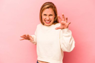 Pembe arka planda izole edilmiş genç beyaz kadın pençelerini kedi taklidi yaparken gösteriyor, agresif bir hareket..