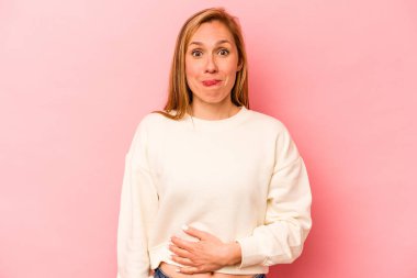 Genç beyaz kadın pembe arka planda izole edilmiş karnına dokunuyor, nazikçe gülümsüyor, yemek yiyor ve tatmin oluyor..