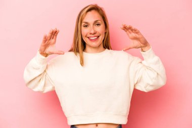 Pembe arka planda izole edilmiş beyaz bir kadın elinde avuç içi bir şeyle kameraya sunuyor..