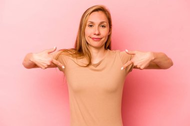 Pembe arka planda izole edilmiş genç beyaz bir kadın gömlek fotokopisini elle gösteriyor, gururlu ve kendinden emin.