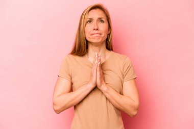 Pembe arka planda soyutlanmış genç beyaz bir kadın el ele tutuşup ağzının kenarında dua ediyor, kendinden emin hissediyor..