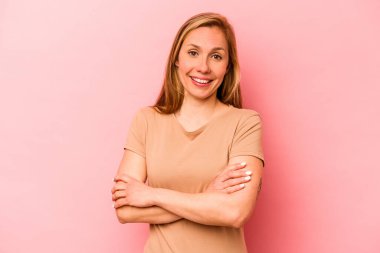 Pembe arka planda soyutlanmış genç beyaz kadın kendini güvende hissediyor, kararlılıkla kollarını kavuşturuyor..