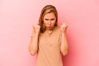Pembe arka planda izole edilmiş genç beyaz kadın yumruğunu kameraya gösteriyor, agresif yüz ifadesi..