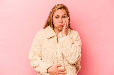 Pembe arka planda izole edilmiş genç beyaz kadın yanakları patlatıyor, yorgun bir ifade takınıyor. Yüz ifadesi kavramı.