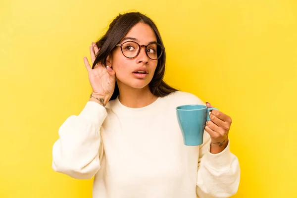 Ung Latinamerikansk Kvinna Håller Mugg Isolerad Gul Bakgrund Försöker Lyssna — Stockfoto