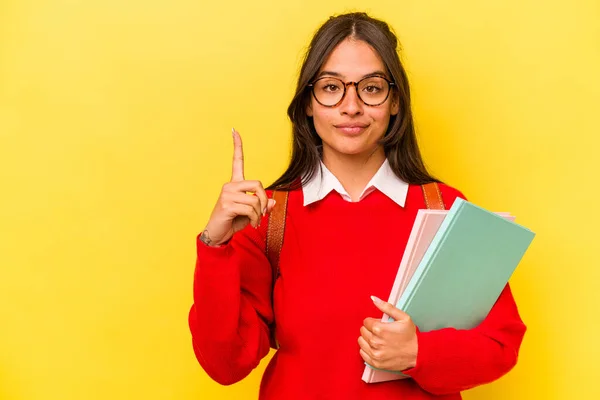 Young student hispanic woman isolated on yellow background showing number one with finger.