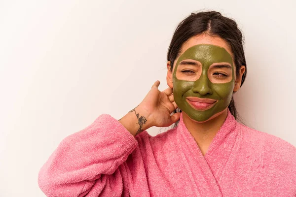 Yüz maskesi takan genç İspanyol kadın beyaz arka planda izole edilmiş kafasının arkasına dokunuyor, düşünüyor ve bir seçim yapıyor..