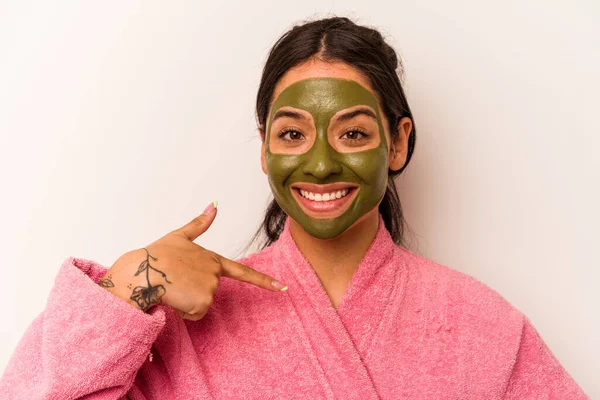 Yüz maskesi takan genç İspanyol bir kadın beyaz arka planda izole edilmiş. Elle bir gömlek fotokopi alanını işaret ediyor. Gururlu ve kendinden emin.