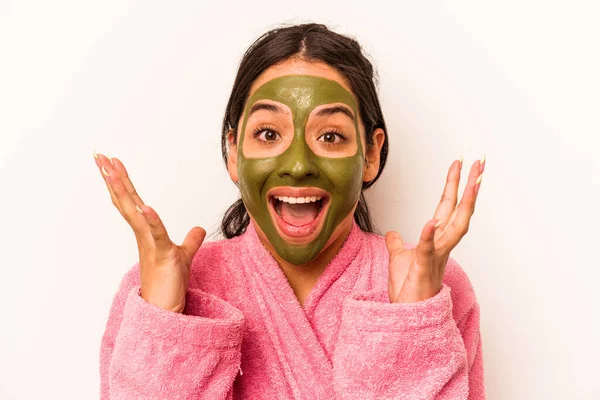 Beyaz arka planda izole edilmiş yüz maskesi takan genç İspanyol kadın hoş bir sürpriz alıyor, heyecanlı ve el kaldırıyor..