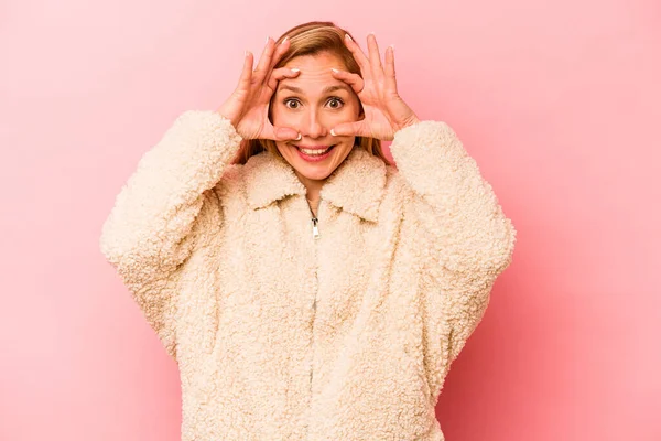 Pembe arka planda izole edilmiş genç beyaz kadın bir başarı fırsatı bulmak için gözlerini açık tutuyor..