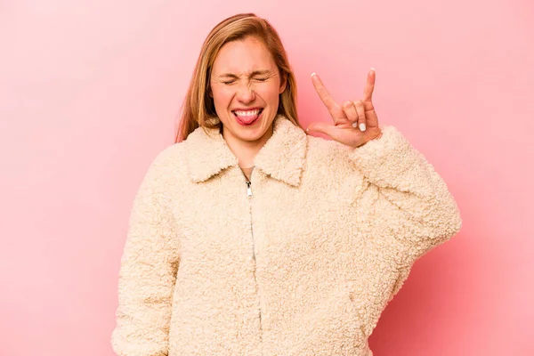 Pembe arka planda izole edilmiş genç beyaz kadın parmaklarıyla taş hareketi gösteriyor.