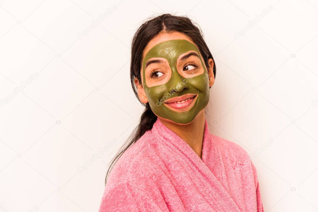 Young hispanic woman wearing a facial mask isolated on white background looks aside smiling, cheerful and pleasant.