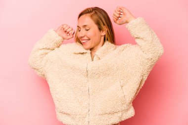 Pembe arka planda soyutlanmış genç beyaz bir kadın özel bir günü kutluyor, atlıyor ve enerjiyle kollarını kaldırıyor..