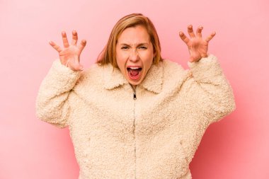 Pembe arka planda izole edilmiş genç beyaz kadın pençelerini kedi taklidi yaparken gösteriyor, agresif bir hareket..