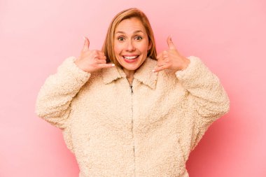 Pembe arka planda izole edilmiş genç beyaz kadın parmaklarıyla bir cep telefonu hareketi gösteriyor..