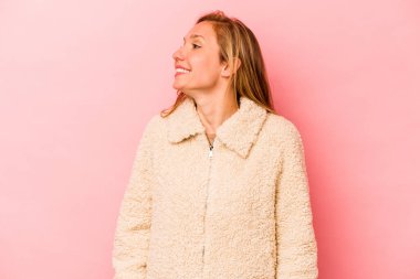 Genç beyaz kadın pembe arka planda izole edilmiş rahat ve mutlu bir şekilde gülüyor, boynunda dişlerini gösteriyor..