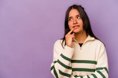 Mor arka planda izole edilmiş genç İspanyol kadın şüpheli ve şüpheci bir ifadeyle yana bakıyor..