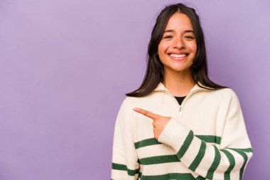 Mor arka planda izole edilmiş genç İspanyol kadın gülümsüyor ve boş alanda bir şeyler gösteriyor..