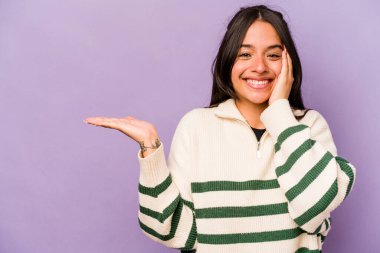 Mor arka planda izole edilmiş genç İspanyol kadın avuç içinde fotokopi alanı tutuyor, el üstünde tutuyor. Şaşırmış ve mutlu..