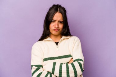 Mor arka planda izole edilmiş, hoşnutsuzca kaşlarını çatmış, kollarını kavuşturmuş genç bir İspanyol kadın..