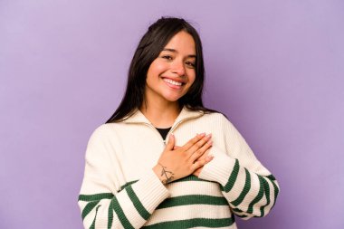 Mor arka planda izole edilmiş genç İspanyol kadın, avuçlarını göğsüne bastıran dostça bir ifadeye sahiptir. Aşk konsepti.