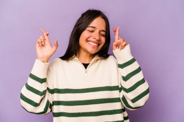 Mor arka planda izole edilmiş genç İspanyol kadın şans dilemek için parmaklarını çapraz yapıyor.