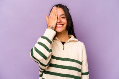 Mor arka planda izole edilmiş genç İspanyol kadın yüzünün yarısını avuç içiyle kaplayarak eğleniyor..